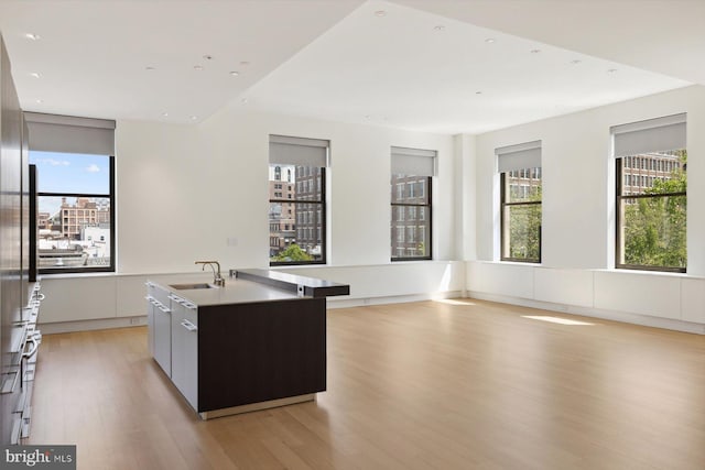 kitchen featuring modern cabinets, light countertops, a large island with sink, light wood-style floors, and a sink