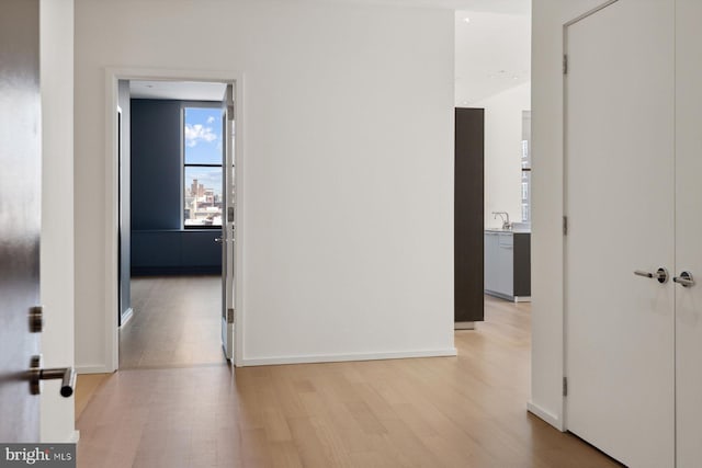 hall with a sink, light wood-style flooring, and baseboards