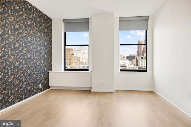 empty room featuring baseboards, wallpapered walls, light wood-type flooring, and a city view