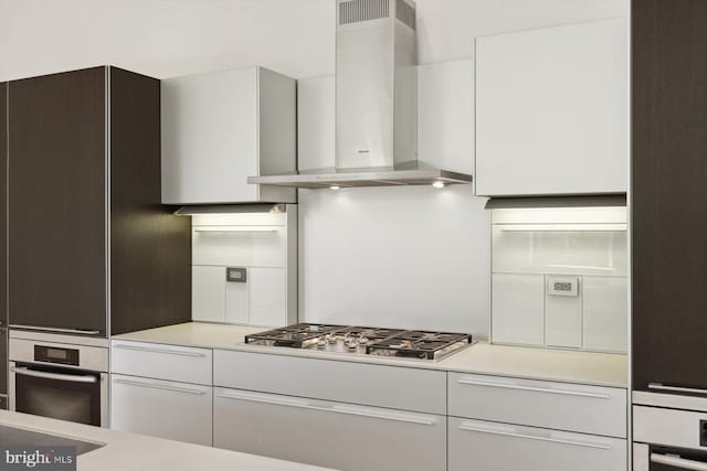 kitchen featuring stainless steel appliances, wall chimney exhaust hood, white cabinets, and light countertops