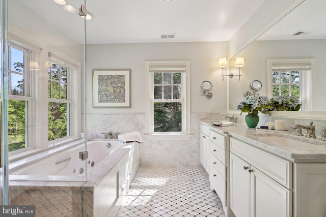 bathroom with a relaxing tiled tub, vanity, tile patterned flooring, and tile walls