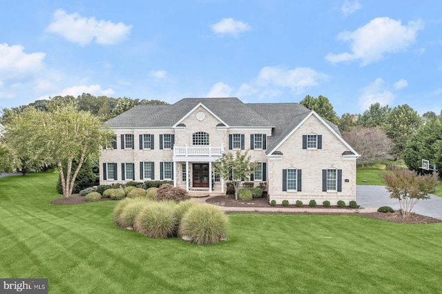 colonial-style house with brick siding, a balcony, and a front lawn
