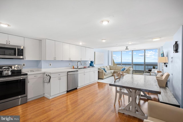 kitchen with white cabinets, a water view, appliances with stainless steel finishes, sink, and light hardwood / wood-style floors