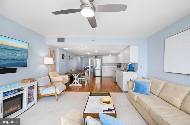 living room with sink, light hardwood / wood-style floors, and ceiling fan