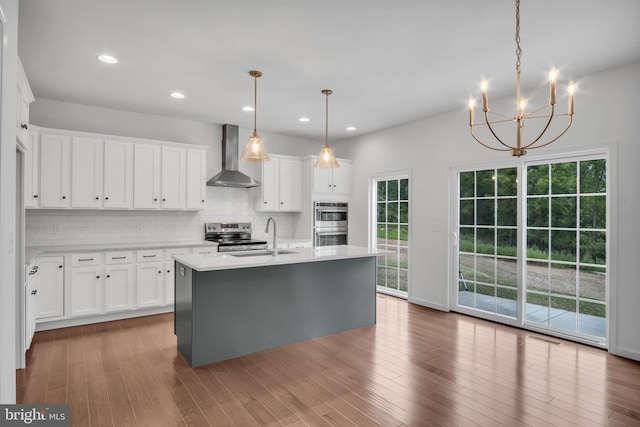 kitchen with light countertops, a sink, wall chimney range hood, and white cabinetry