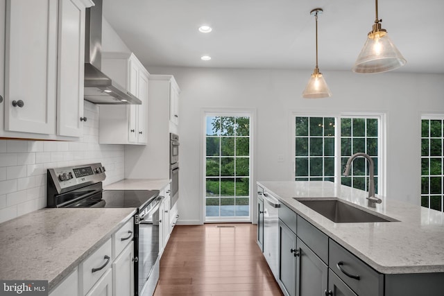 kitchen featuring appliances with stainless steel finishes, white cabinetry, a sink, an island with sink, and wall chimney exhaust hood