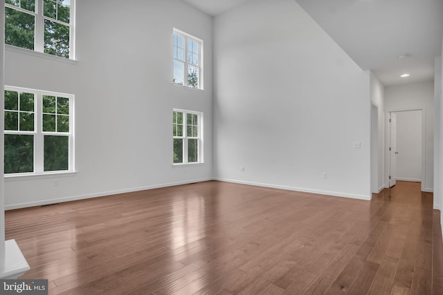 unfurnished living room featuring a high ceiling, wood finished floors, visible vents, and baseboards