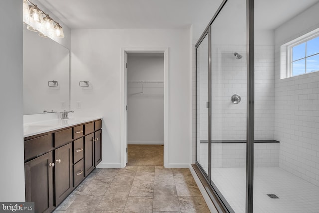 bathroom with double vanity, baseboards, a walk in closet, a shower stall, and a sink