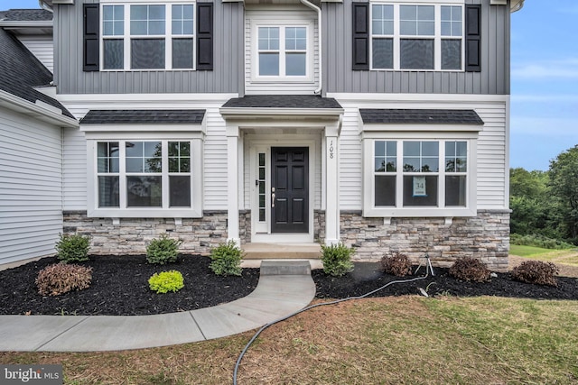 doorway to property with stone siding, a yard, board and batten siding, and roof with shingles