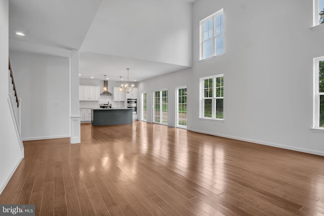 unfurnished living room with recessed lighting, wood finished floors, baseboards, stairs, and an inviting chandelier