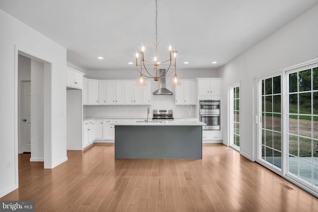 kitchen featuring light countertops, hanging light fixtures, a kitchen island with sink, and white cabinets