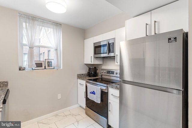 kitchen with appliances with stainless steel finishes, dark stone counters, white cabinetry, and light tile floors