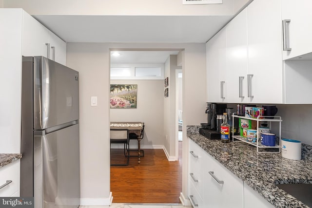 kitchen with dark stone countertops, white cabinets, stainless steel fridge, and hardwood / wood-style floors