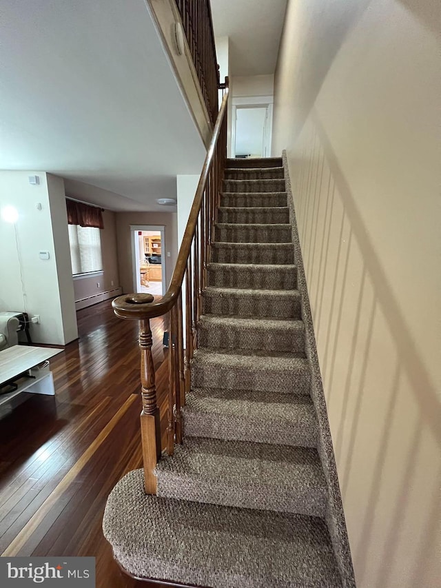 staircase featuring a baseboard heating unit and dark hardwood / wood-style floors