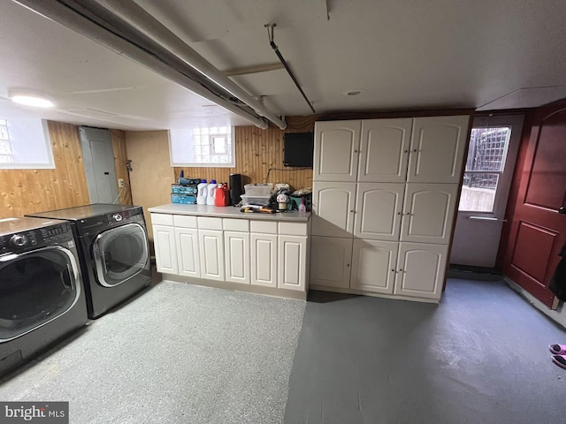 washroom with wood walls, washer and dryer, and cabinets