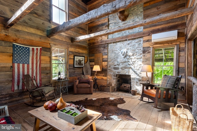 living room featuring an AC wall unit, beam ceiling, a high ceiling, hardwood / wood-style floors, and a stone fireplace