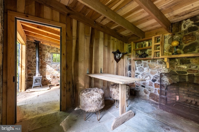 interior space featuring wooden walls, vaulted ceiling with beams, a wood stove, and wood ceiling