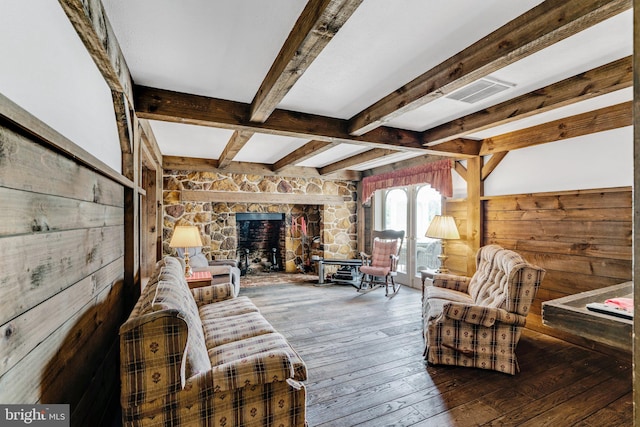 living room with wood-type flooring, beam ceiling, wooden walls, and a stone fireplace