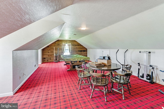 interior space with a textured ceiling, carpet floors, vaulted ceiling, and wooden walls