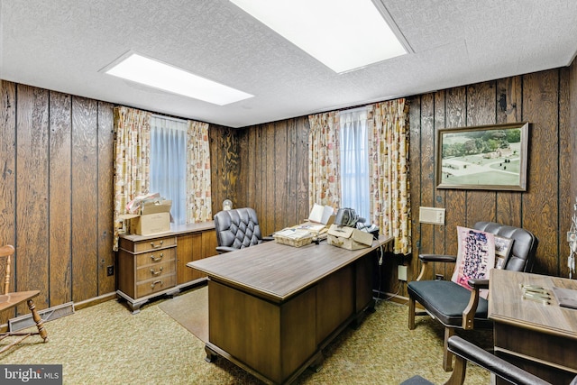 carpeted home office with a skylight, wooden walls, a wealth of natural light, and a textured ceiling