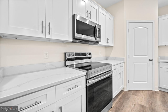 kitchen with light stone counters, white cabinets, stainless steel appliances, and light hardwood / wood-style floors