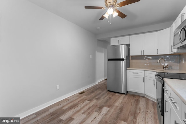 kitchen with appliances with stainless steel finishes, tasteful backsplash, sink, light hardwood / wood-style flooring, and white cabinetry