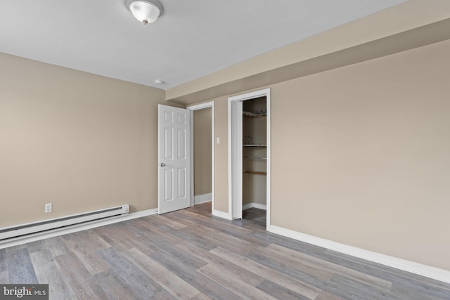 unfurnished bedroom featuring a spacious closet, a closet, light hardwood / wood-style floors, and a baseboard heating unit