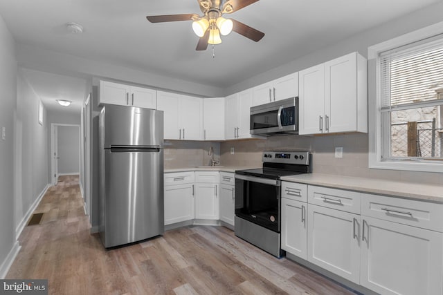 kitchen featuring decorative backsplash, appliances with stainless steel finishes, ceiling fan, light hardwood / wood-style flooring, and white cabinetry