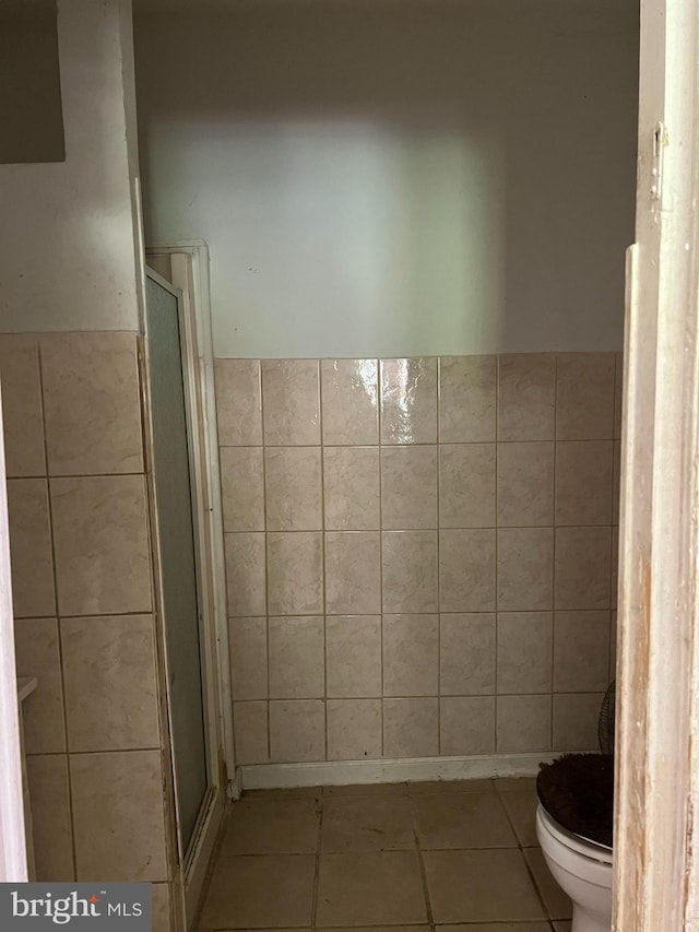 bathroom featuring tile patterned flooring, a shower with shower door, tile walls, and toilet