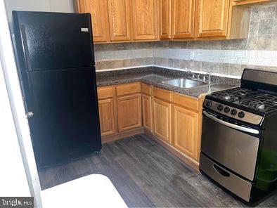 kitchen with dark hardwood / wood-style flooring, sink, black refrigerator, and gas stove