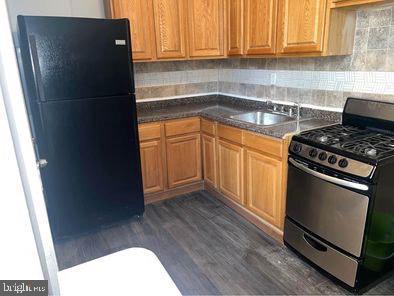 247 S 55th St, Philadelphia, PA 19139 - kitchen with decorative backsplash, dark wood-style flooring, stainless steel gas range, a sink, and freestanding refrigerator