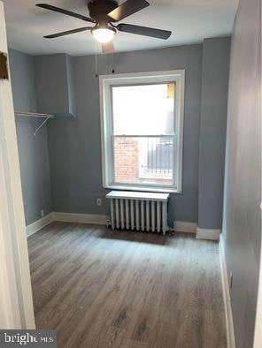 unfurnished room with ceiling fan, hardwood / wood-style floors, and radiator heating unit