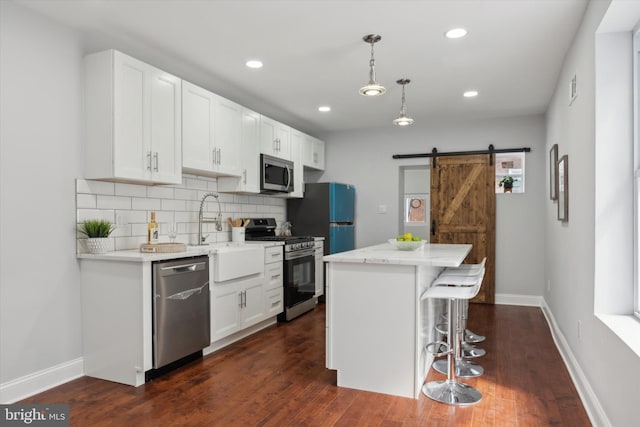 kitchen with white cabinets, appliances with stainless steel finishes, a barn door, and dark hardwood / wood-style floors