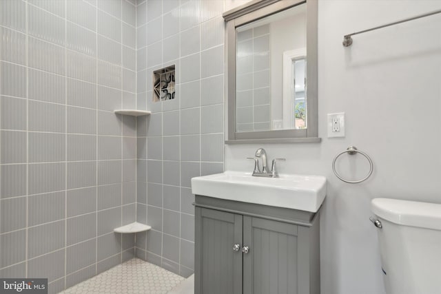 bathroom with tiled shower, vanity, and toilet