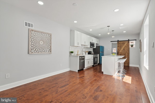 kitchen with tasteful backsplash, a barn door, dark wood-type flooring, and appliances with stainless steel finishes