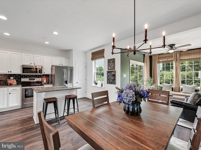 dining space with ceiling fan with notable chandelier and dark wood-type flooring