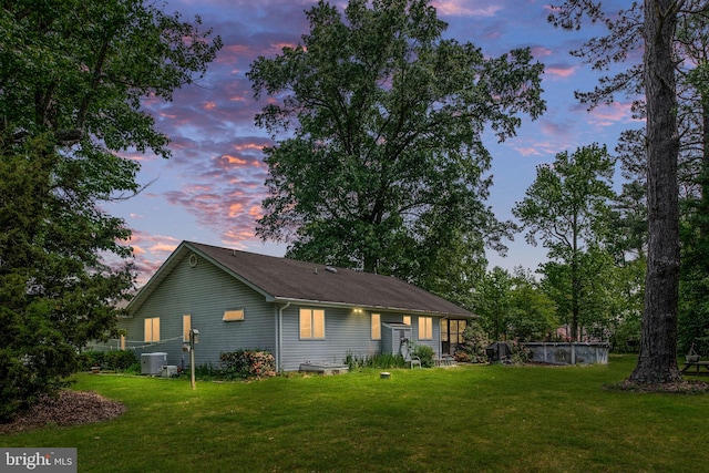 back house at dusk with central AC unit and a yard