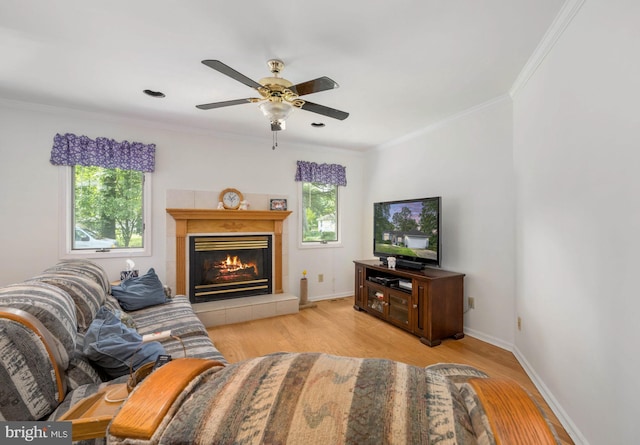 living room with ceiling fan, light wood-type flooring, ornamental molding, and a tiled fireplace