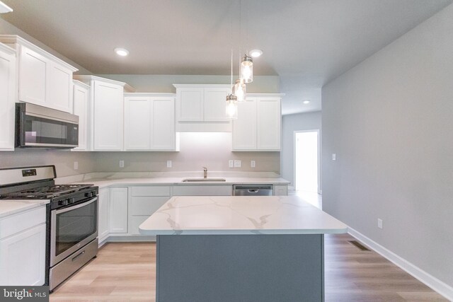 kitchen with pendant lighting, white cabinets, stainless steel appliances, and light wood-type flooring