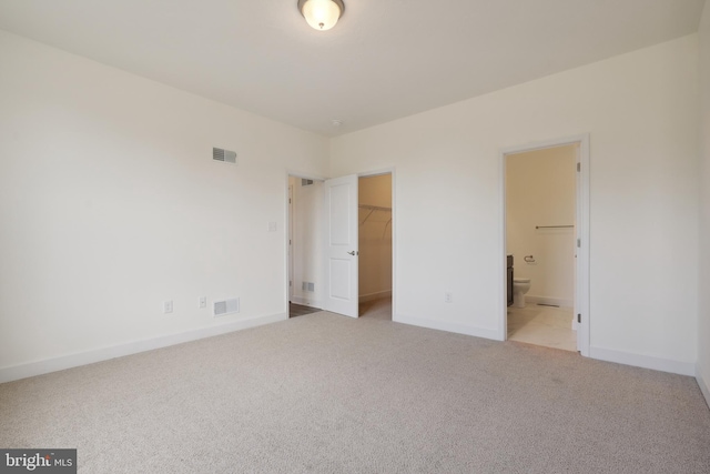 unfurnished bedroom featuring light carpet, a walk in closet, ensuite bathroom, and a closet