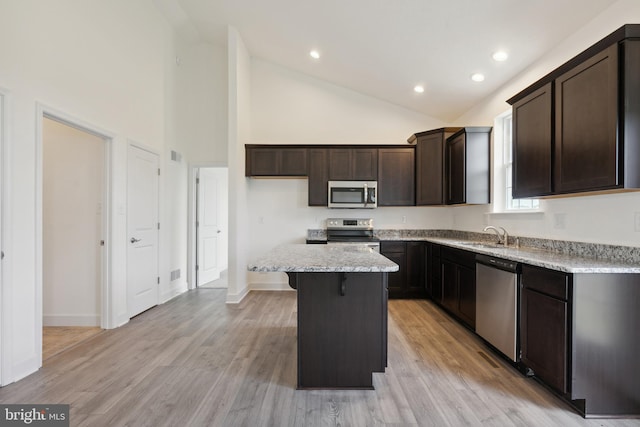 kitchen with high vaulted ceiling, appliances with stainless steel finishes, a center island, dark brown cabinets, and light wood-type flooring