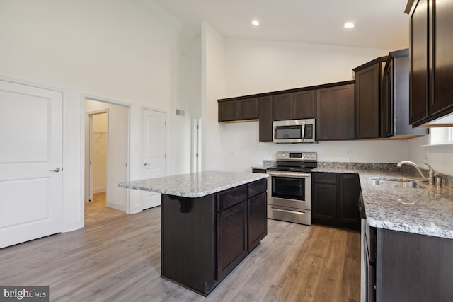 kitchen with light wood-type flooring, light stone counters, stainless steel appliances, high vaulted ceiling, and a center island