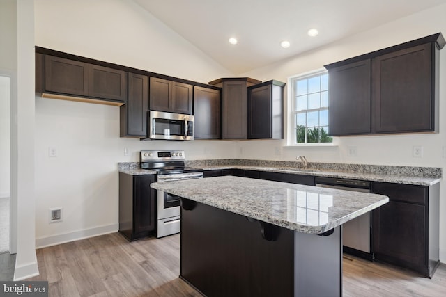 kitchen featuring appliances with stainless steel finishes, vaulted ceiling, sink, light hardwood / wood-style flooring, and a center island