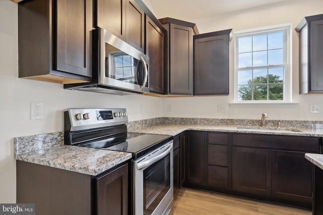 kitchen with sink, appliances with stainless steel finishes, dark brown cabinets, light hardwood / wood-style floors, and light stone countertops