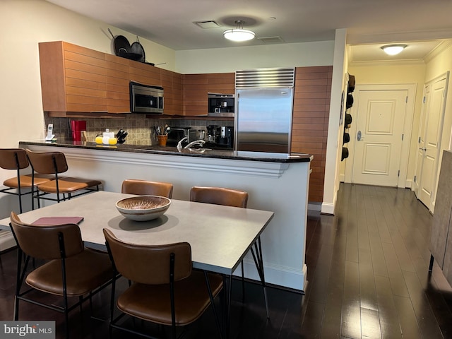 kitchen with dark hardwood / wood-style flooring, kitchen peninsula, stainless steel appliances, and a kitchen breakfast bar