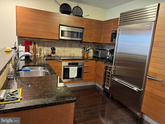 kitchen with dark wood-type flooring, stainless steel appliances, sink, tasteful backsplash, and dark stone counters