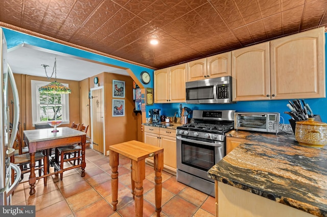 kitchen with light brown cabinetry, light tile patterned floors, stainless steel appliances, and hanging light fixtures