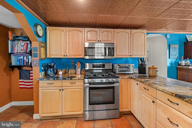 kitchen with appliances with stainless steel finishes, light brown cabinets, and dark stone counters