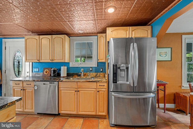 kitchen featuring light brown cabinetry, stainless steel appliances, dark stone counters, and sink