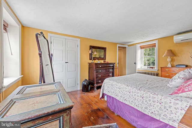 bedroom featuring dark hardwood / wood-style flooring, radiator heating unit, a textured ceiling, and a wall mounted AC